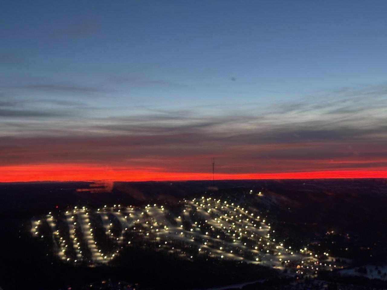 City skyline at dusk with glowing streetlights under a vibrant sunset.