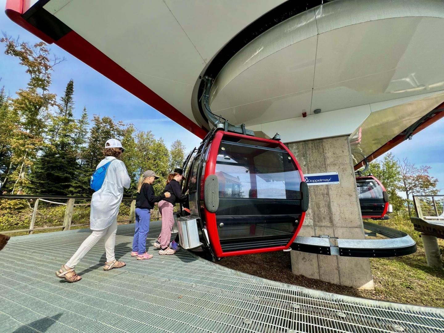 Cable car at station, people boarding, trees in background.