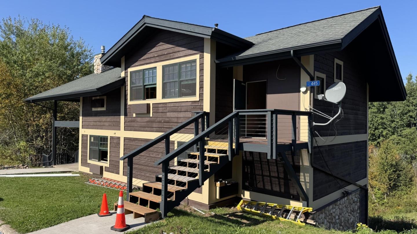 Two-story brown house with beige trim and a satellite dish on a sunny day.