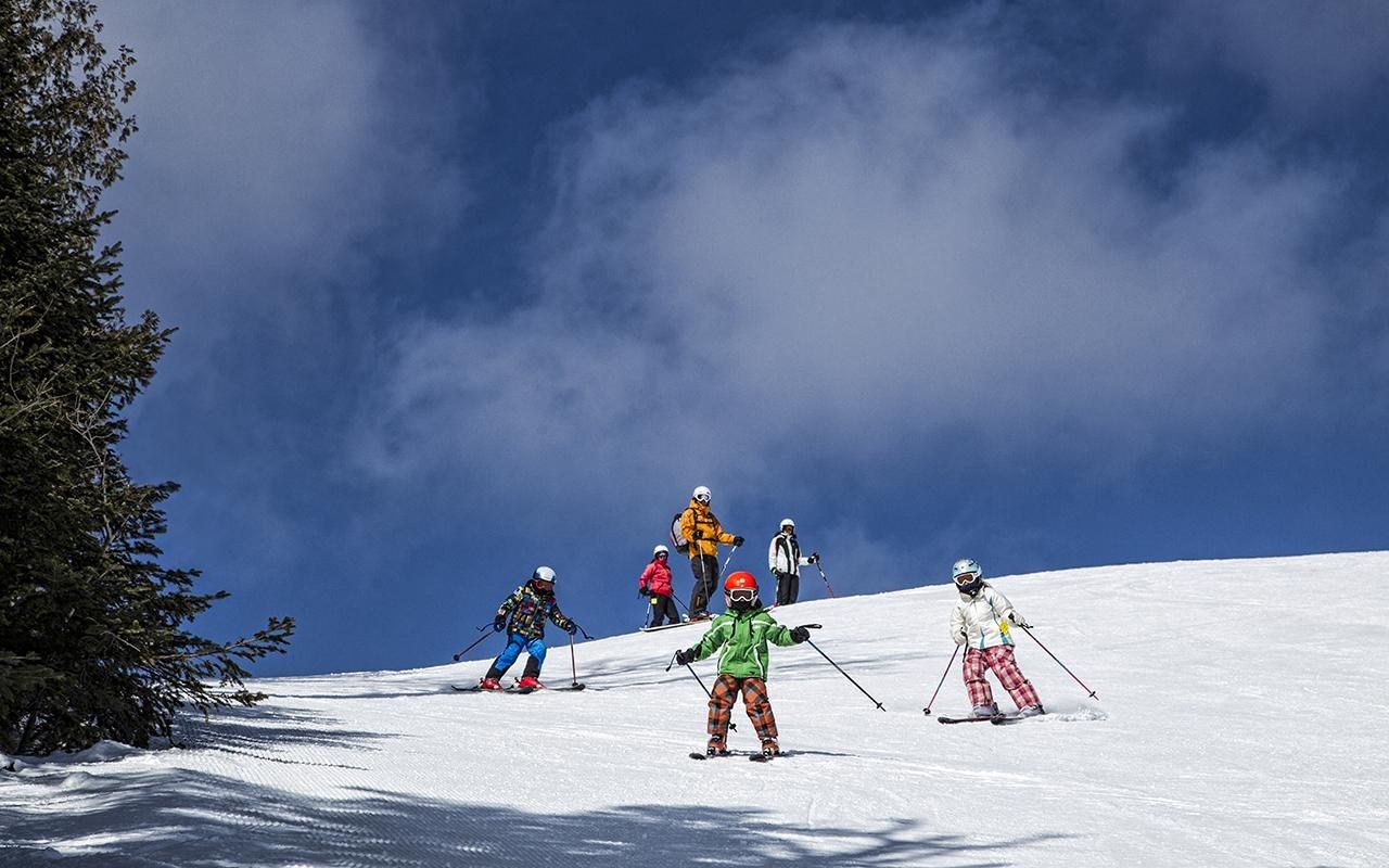 Skiers on a snowy slope under a cloudy blue sky.