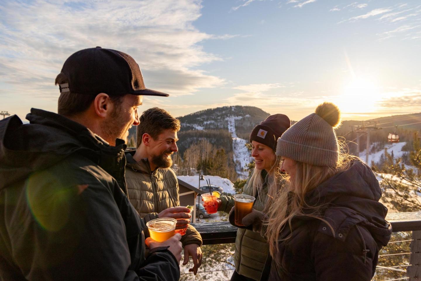 Friends enjoying drinks on a snowy mountain at sunset.