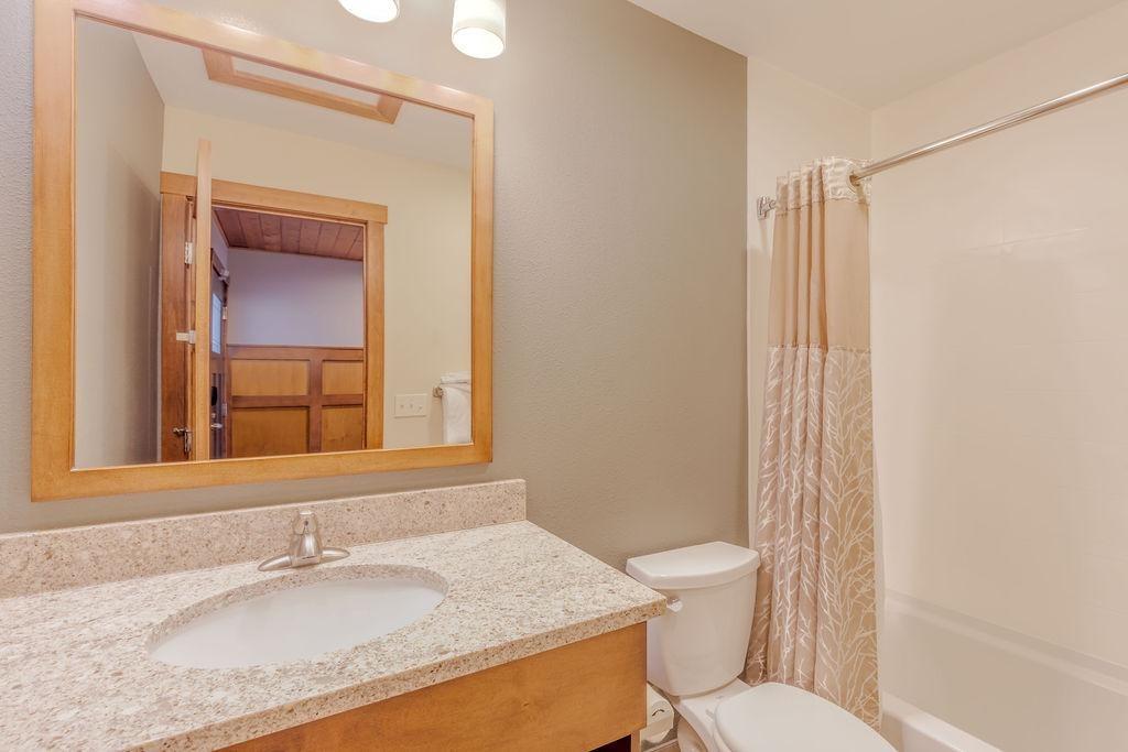 Bathroom with granite countertop, mirror, toilet, and shower with beige curtain.