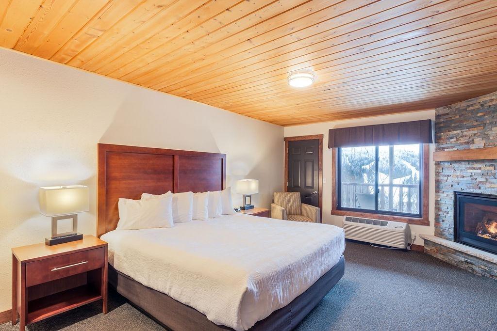 Cozy bedroom with wooden ceiling, large bed, and fireplace.
