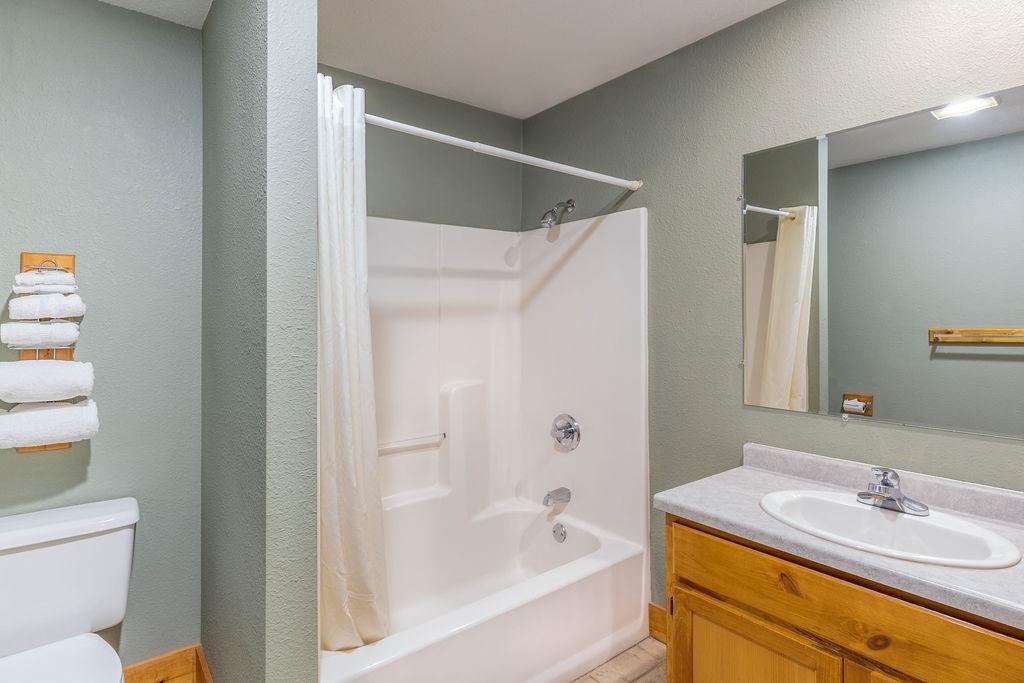 Bathroom with a tub, shower curtain, toilet, and sink with wooden cabinet.