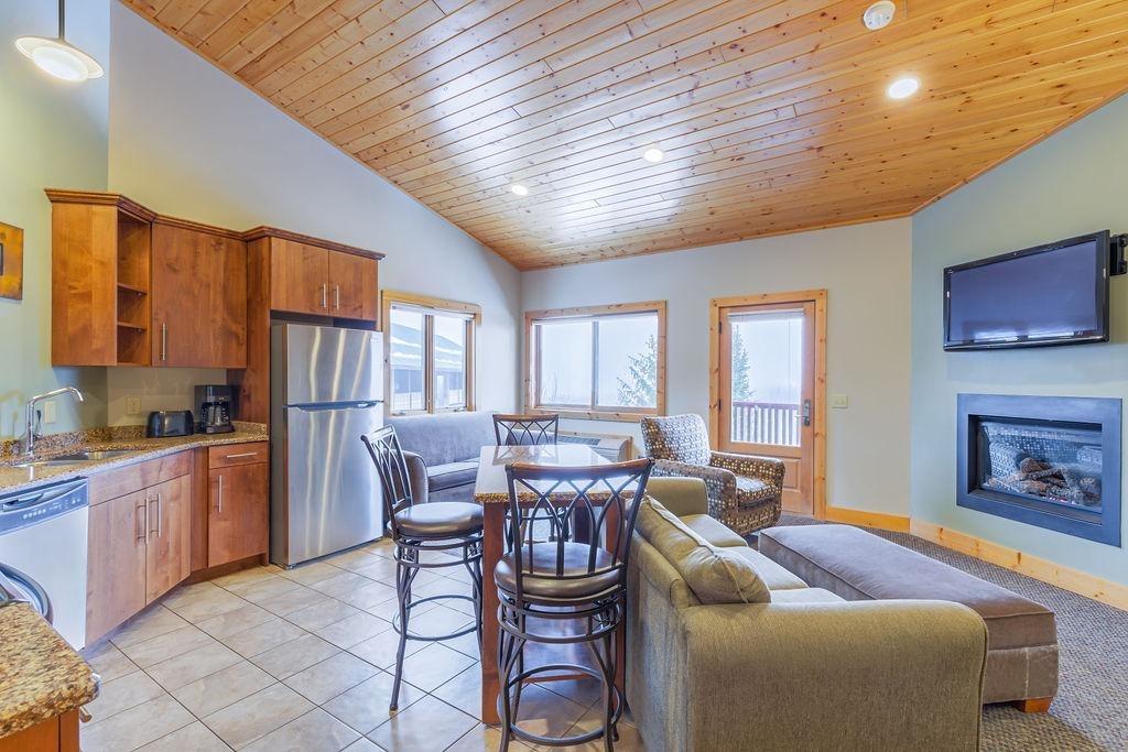 Cozy living room with wooden ceiling, a fireplace, and modern kitchen.
