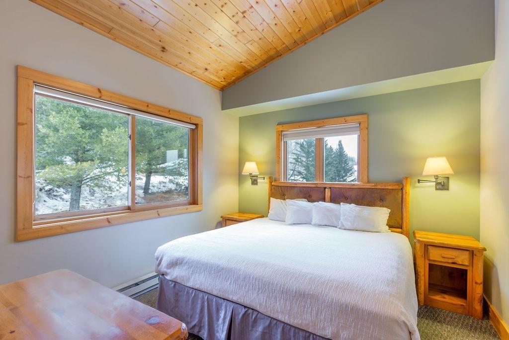 Cozy bedroom with wood ceiling, large window, and double bed.