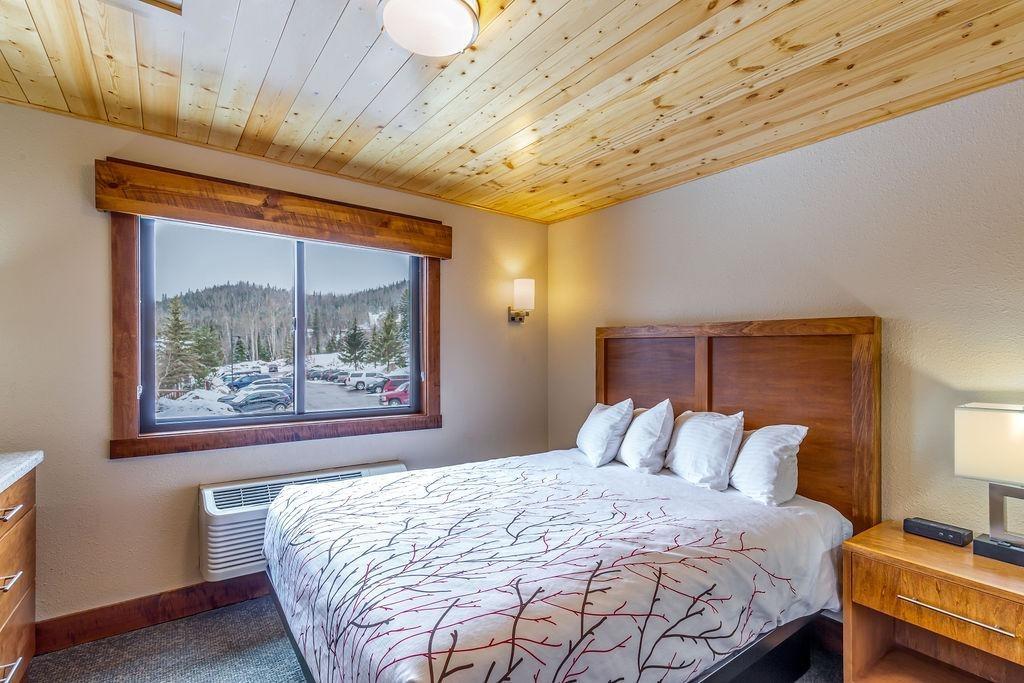 Cozy bedroom with wooden ceiling, mountain view, and a large bed with white pillows.