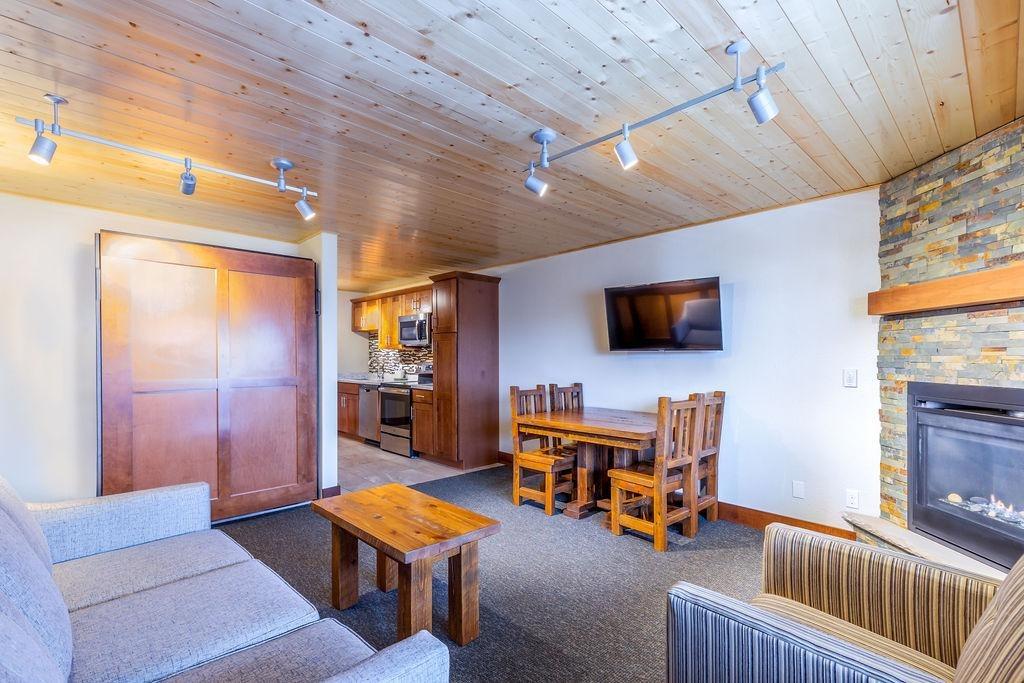 Cozy living room with wooden ceiling, couch, TV, fireplace, and dining table.