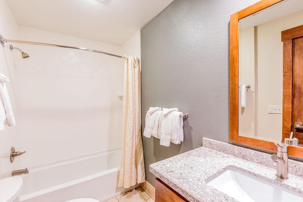 Bright bathroom with granite countertop, large mirror, and shower-tub combination.