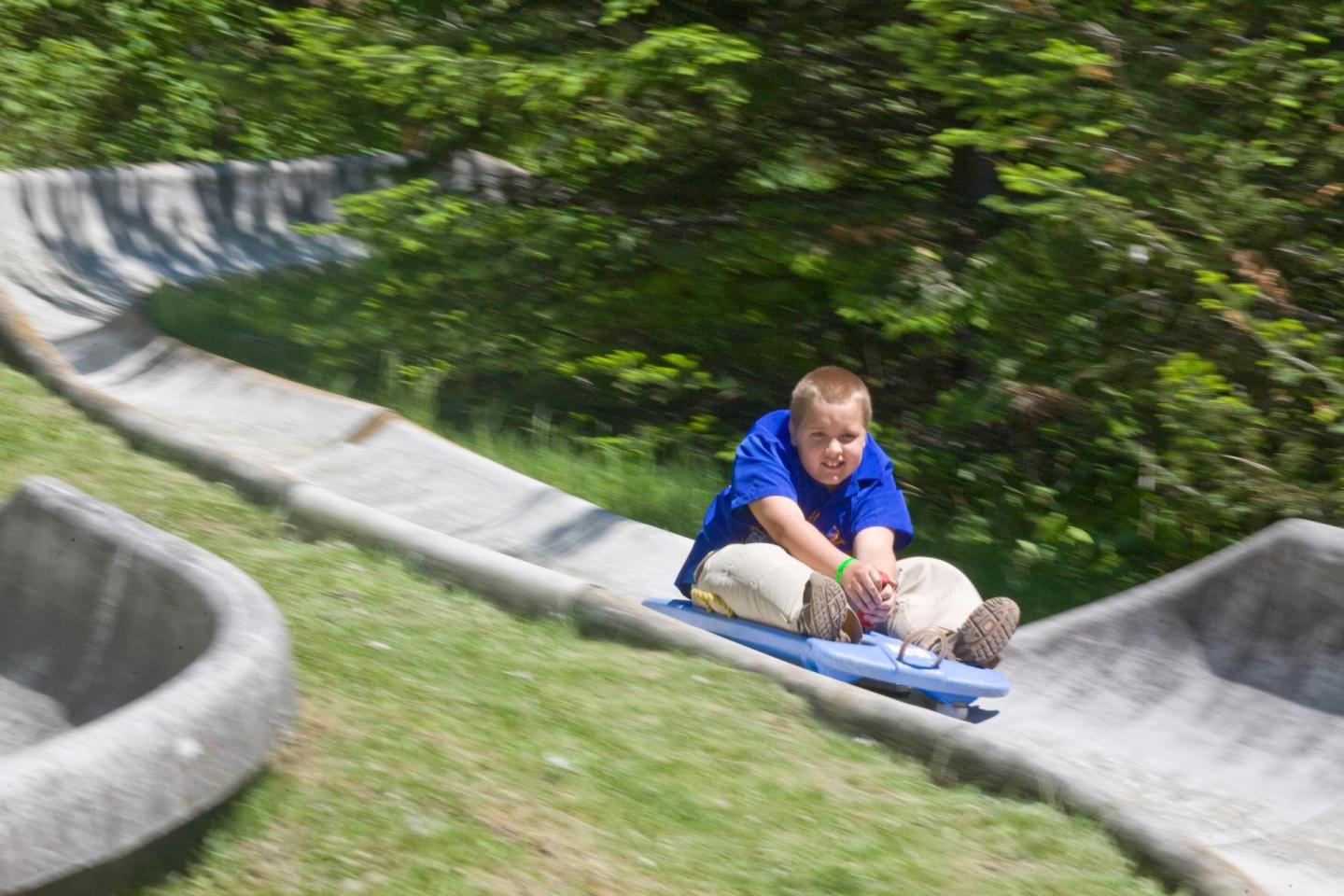 Child in blue shirt sliding down an outdoor concrete slide.