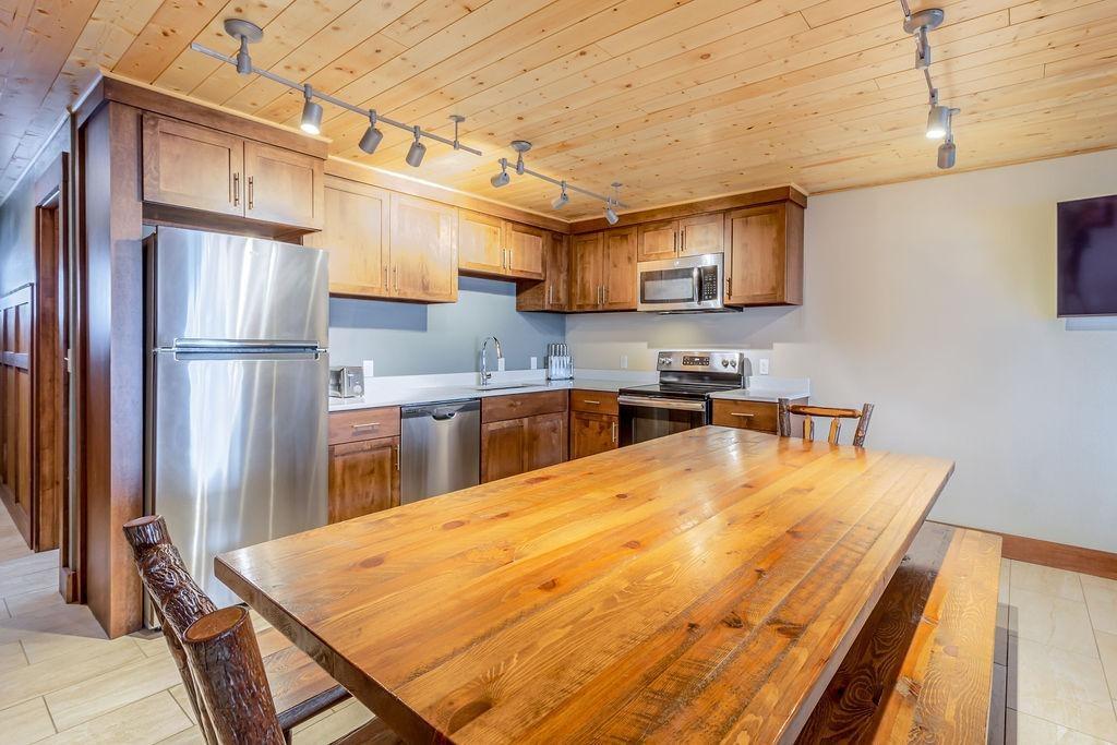 Wooden kitchen with dining table, stainless appliances, and warm lighting.
