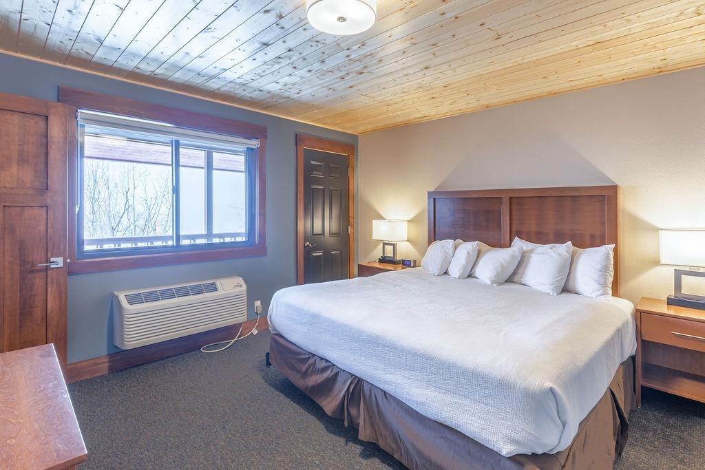 A cozy bedroom with a large bed, wooden ceiling and furniture, soft lighting.