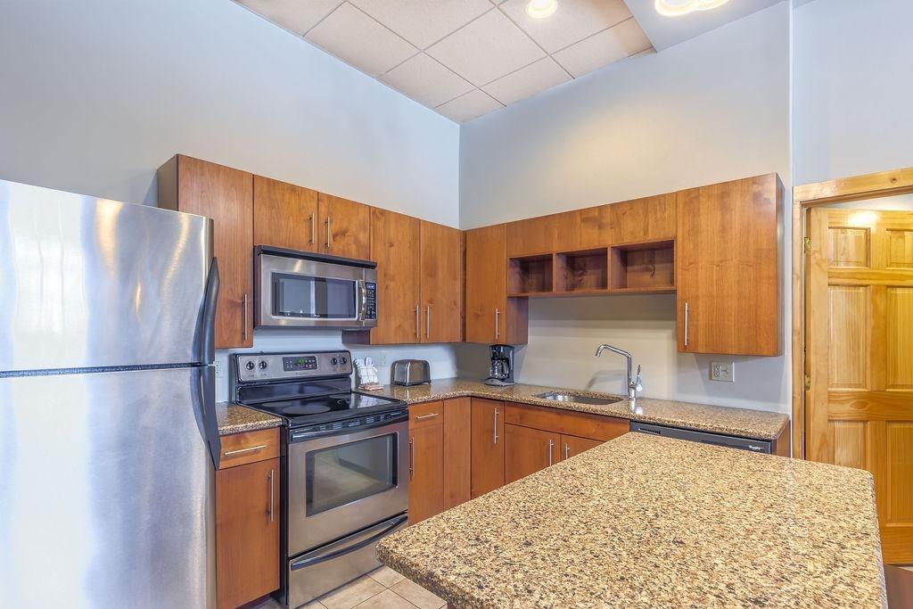Modern kitchen with wooden cabinets, granite island, stainless steel appliances.