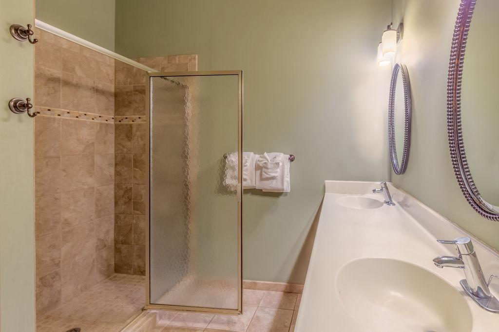 Bathroom with glass shower, double sink, and beige tiles.