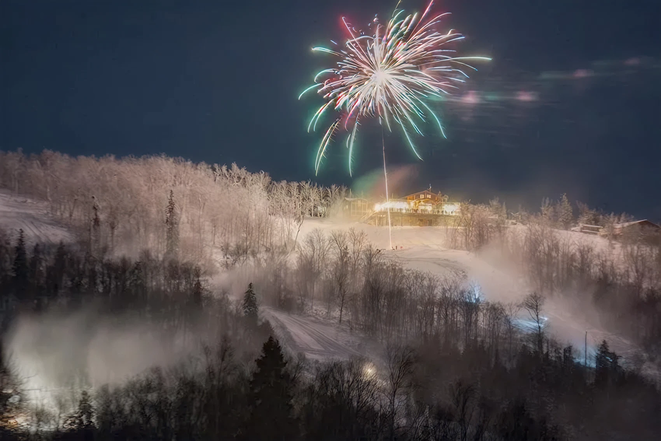 Fireworks burst over snowy hills at night.