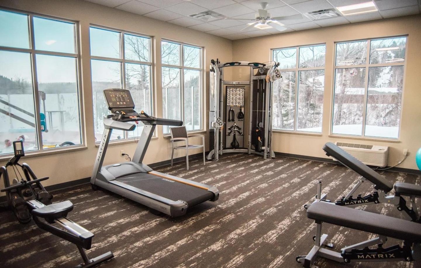 Fitness room with gym equipment and large windows showing a snowy view.