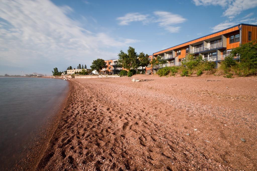 Sandy beach with red buildings and greenery under a blue sky.