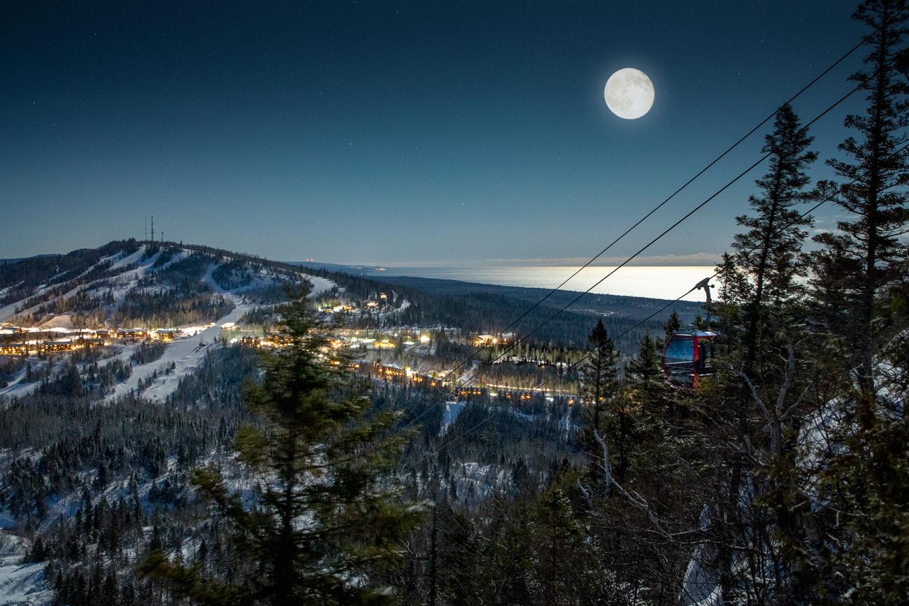 Moonlit snowy mountain landscape with distant city lights.
