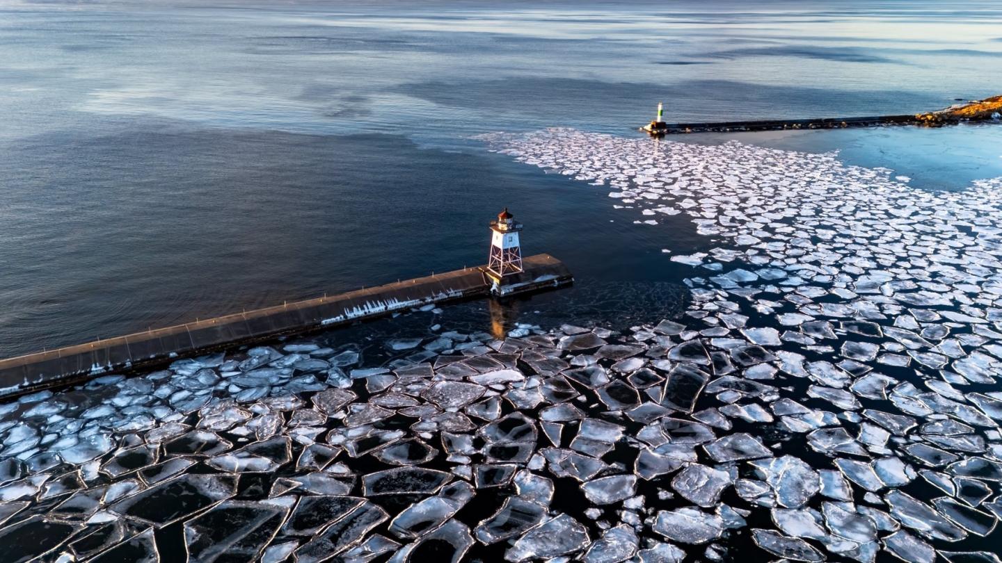 Aerial view of a person standing on a snowy pier with floating ice sheets in water.