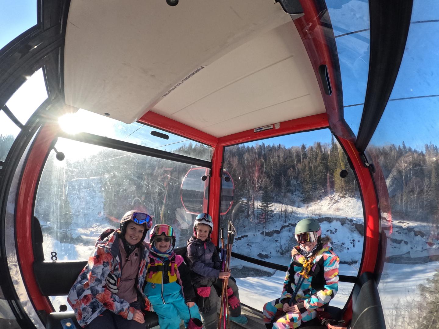 Family in ski gear inside a gondola, snowy landscape outside.