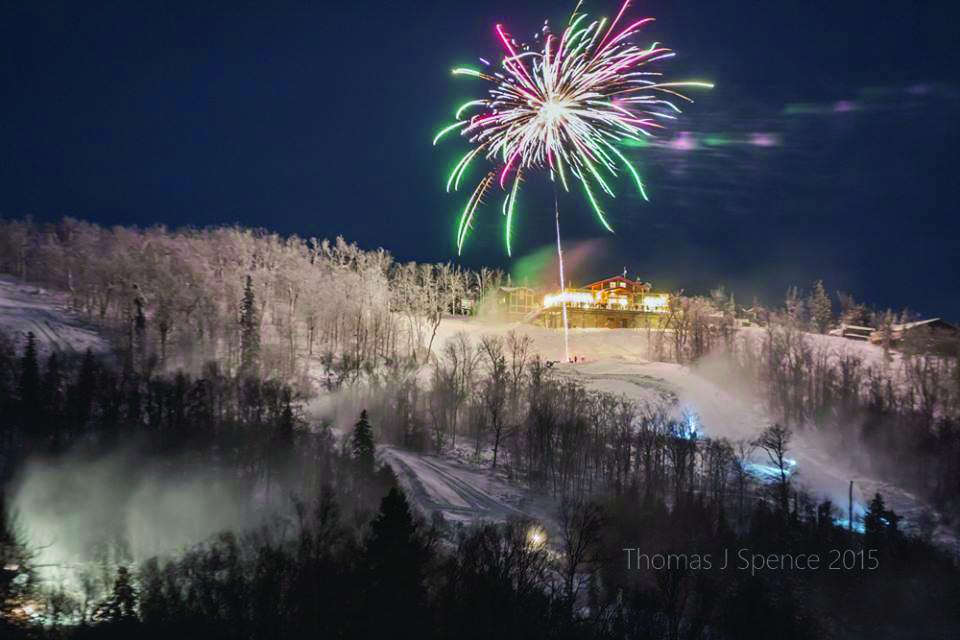 Fireworks exploding over a snowy, illuminated hill at night.