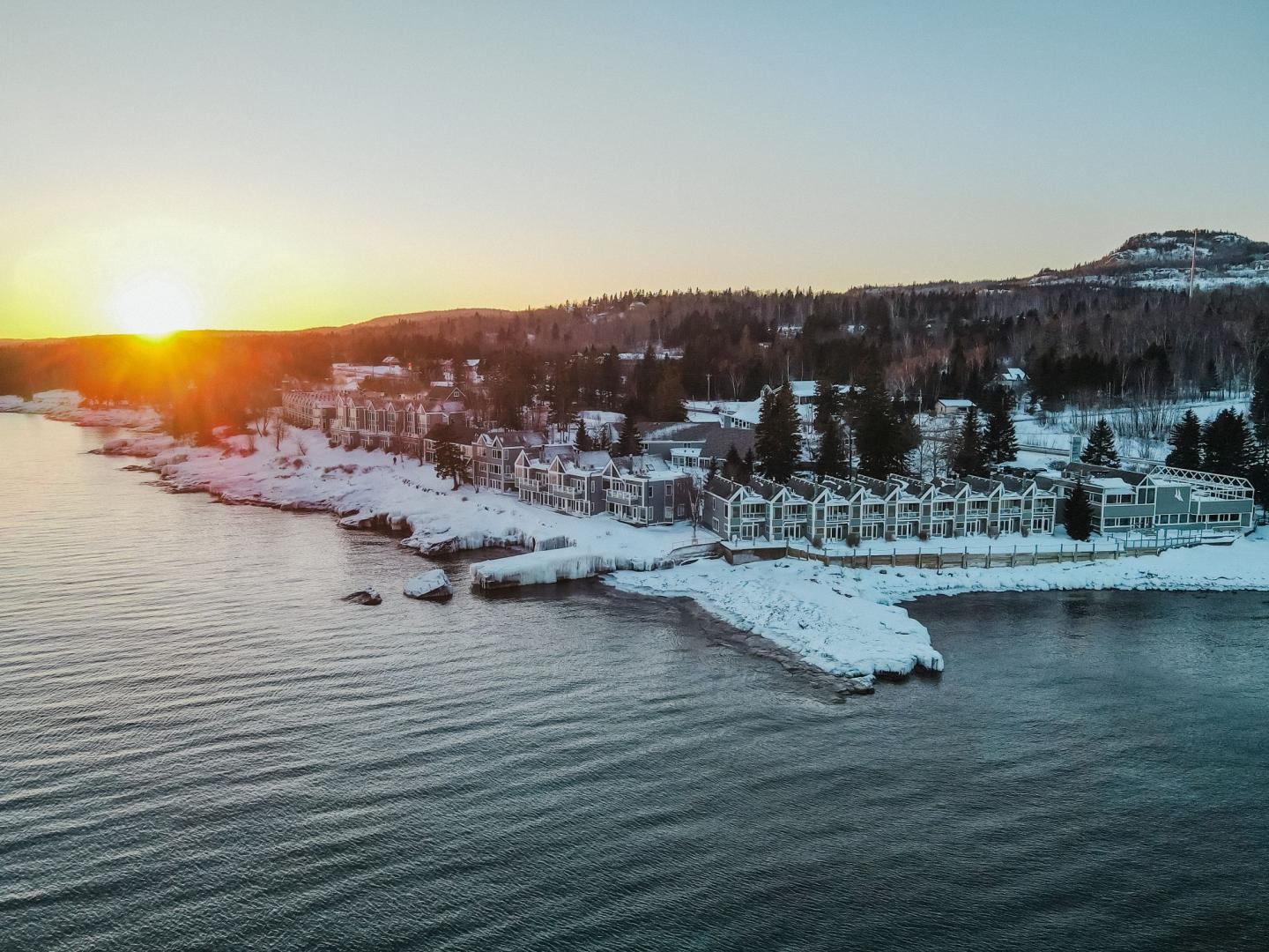 Sunset over snowy lakeside town with distant hills.