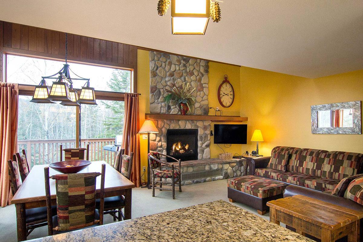 Cozy living room with a stone fireplace, couch, and dining table by a large window.