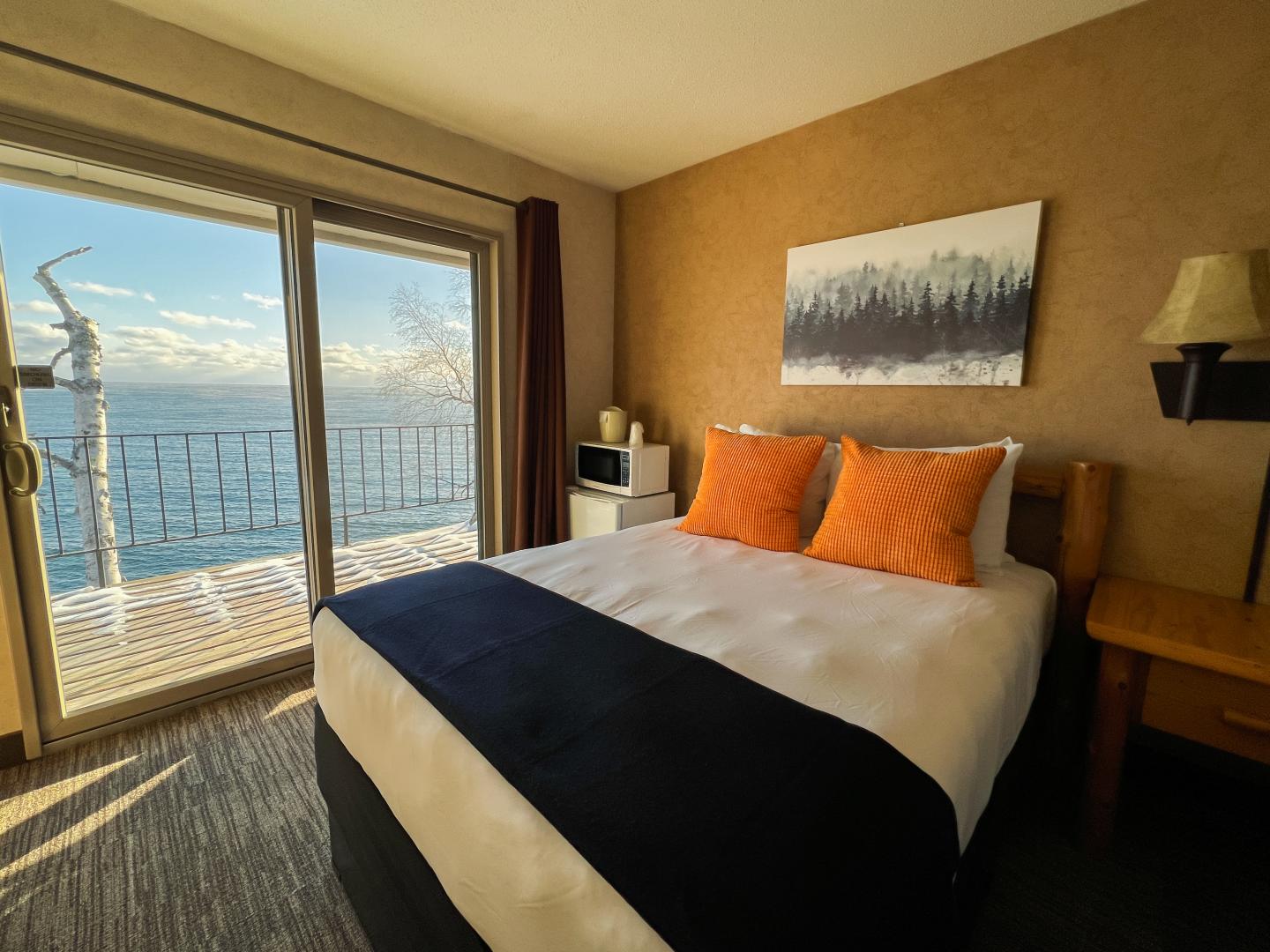 Cozy bedroom with lake view, orange pillows, and snowy balcony.