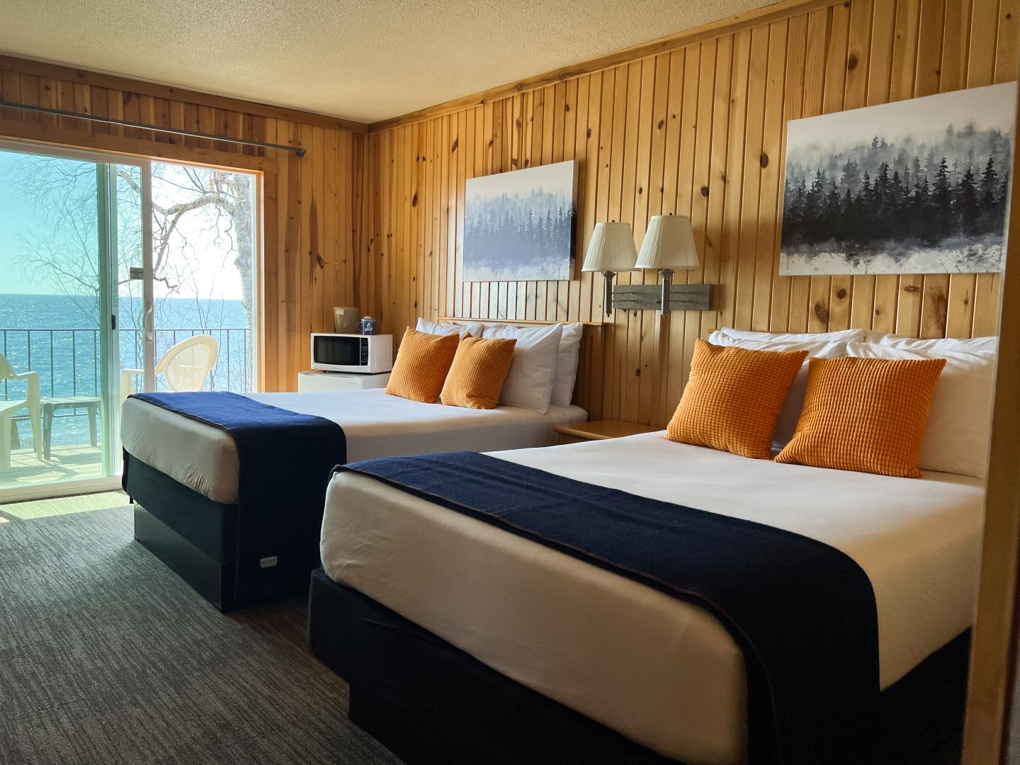 Cozy wood-paneled hotel room with two beds and a lake view balcony.