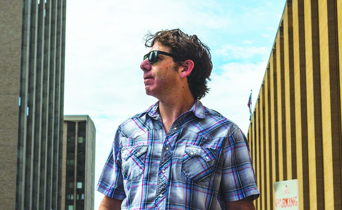 Man in sunglasses walking between tall city buildings.