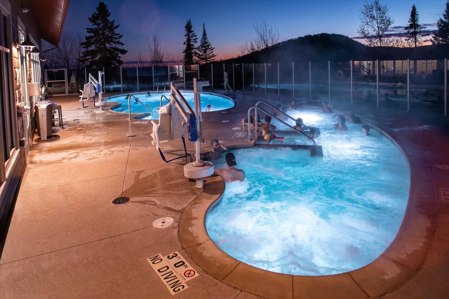 Outdoor heated pool with steam rising at twilight, surrounded by snowy landscape.