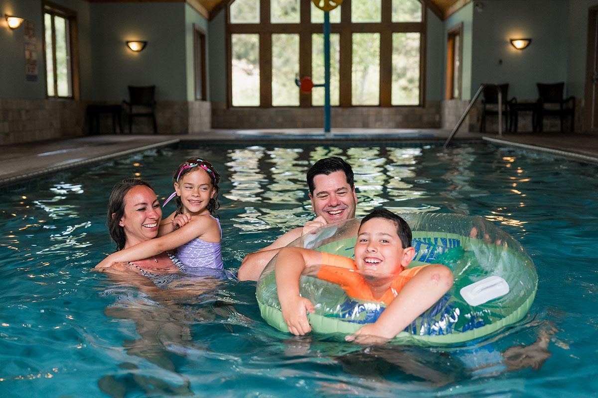 Family swimming in an indoor pool, two children with floats, smiling.