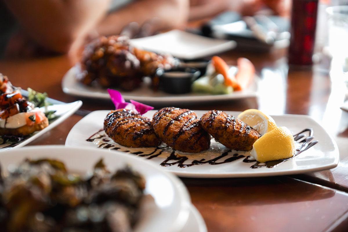 Plated dessert with chocolate drizzle, lemon wedges, and purple flower.