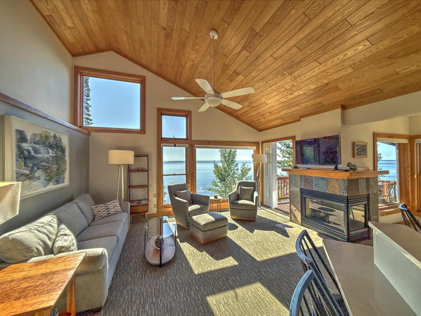 Cozy living room with large windows, wooden ceiling, and lake view.