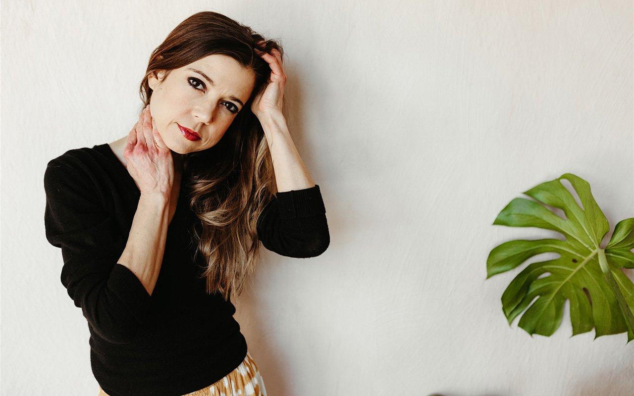 Woman in black sweater posing beside a green plant.