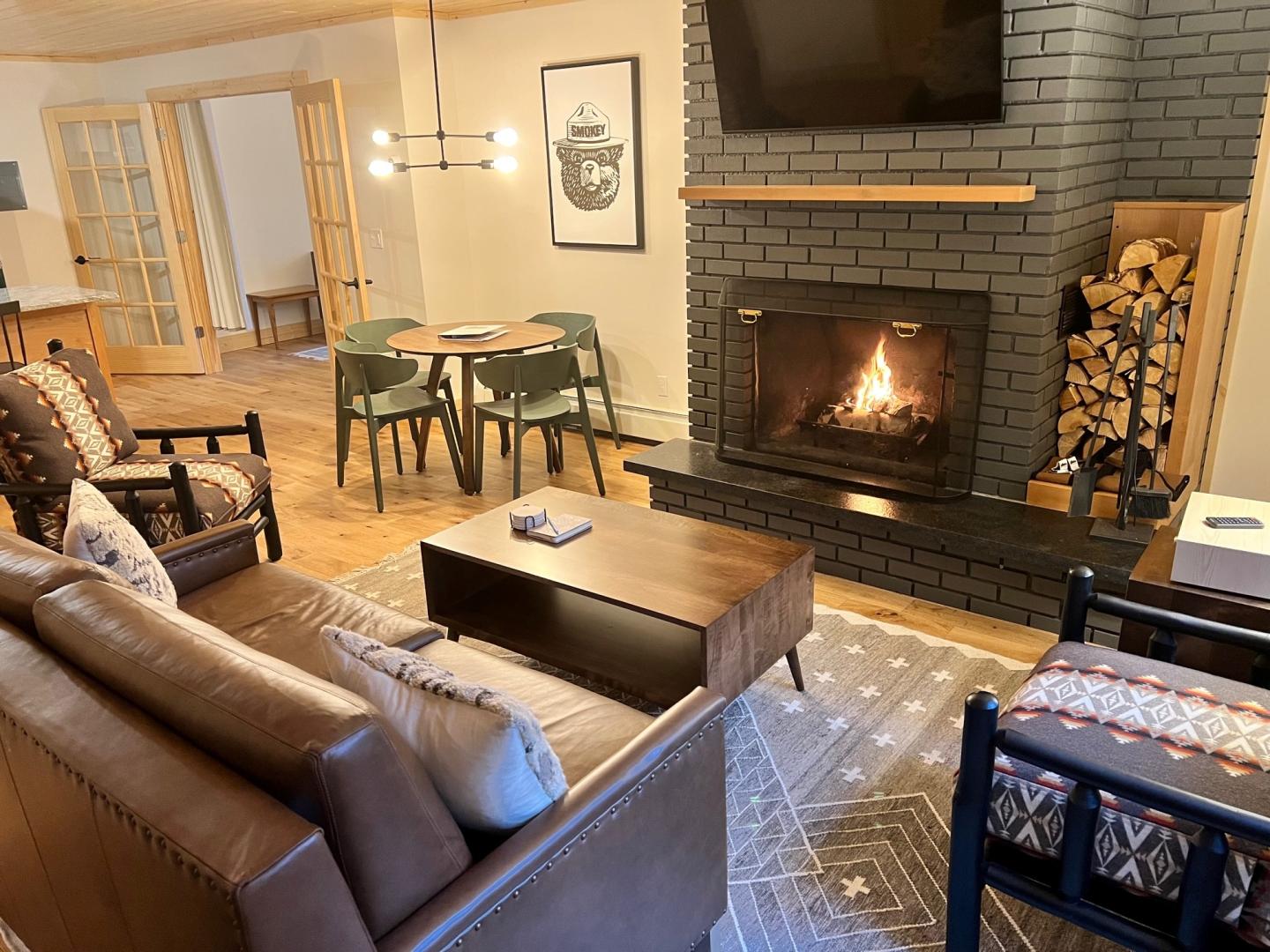 Cozy living room with lit fireplace, sofa, chairs, and dining table.
