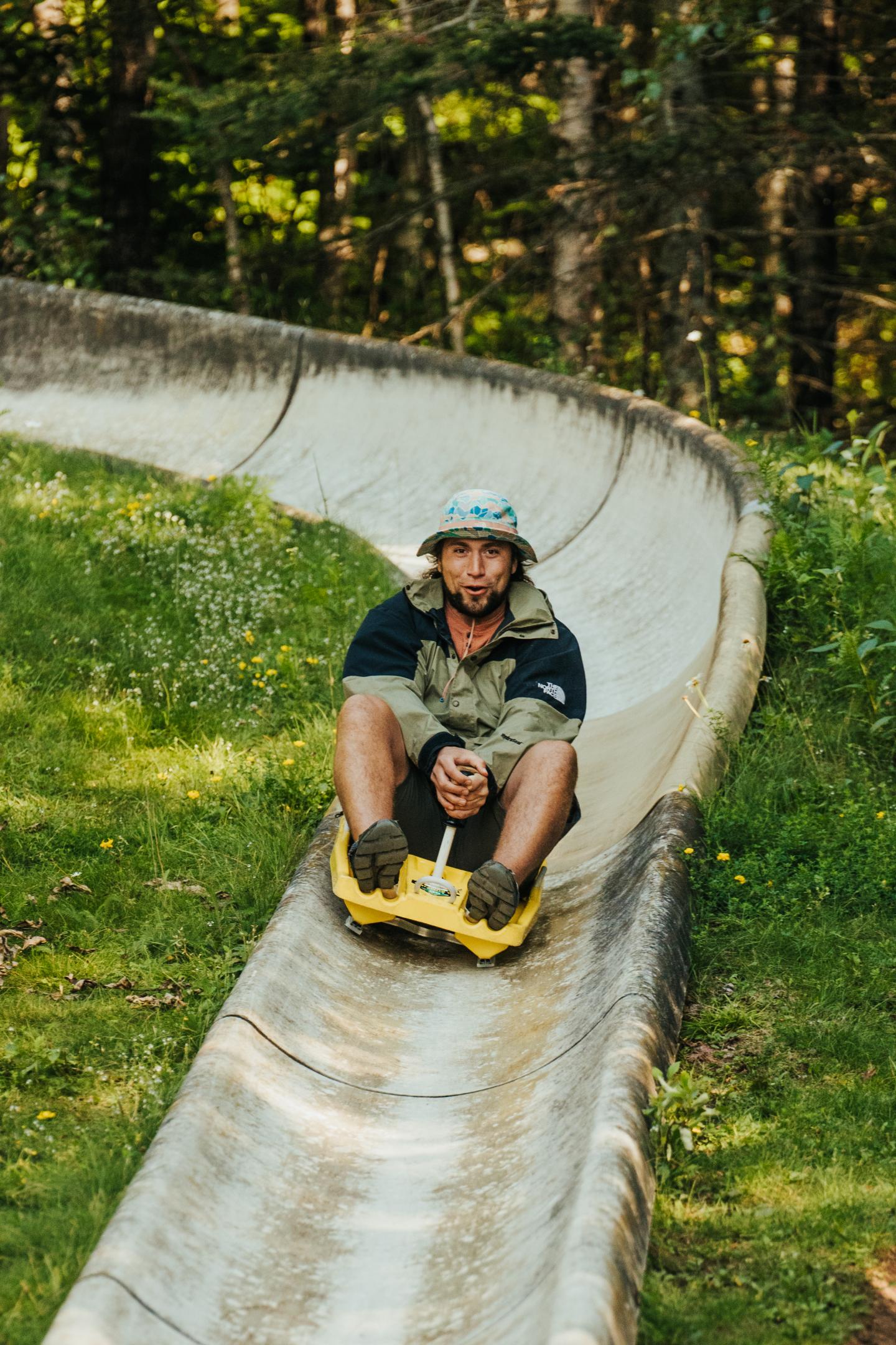 Man sliding down a concrete luge track in a forest setting.