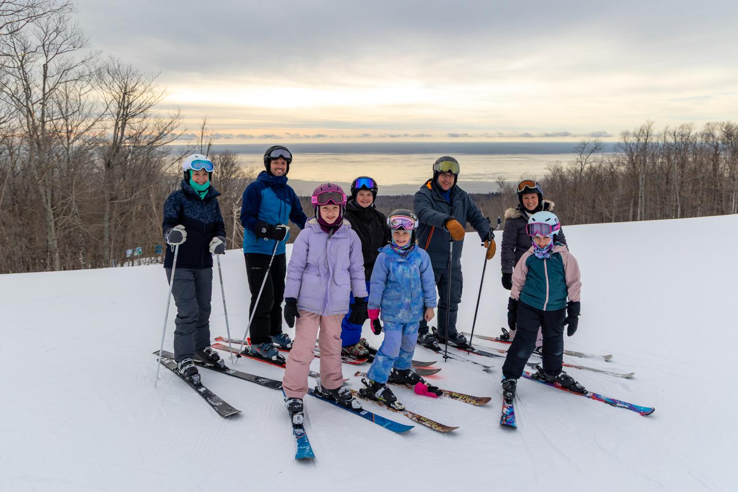 Family of skiers poses on a snowy slope with a cloudy sky and distant trees.