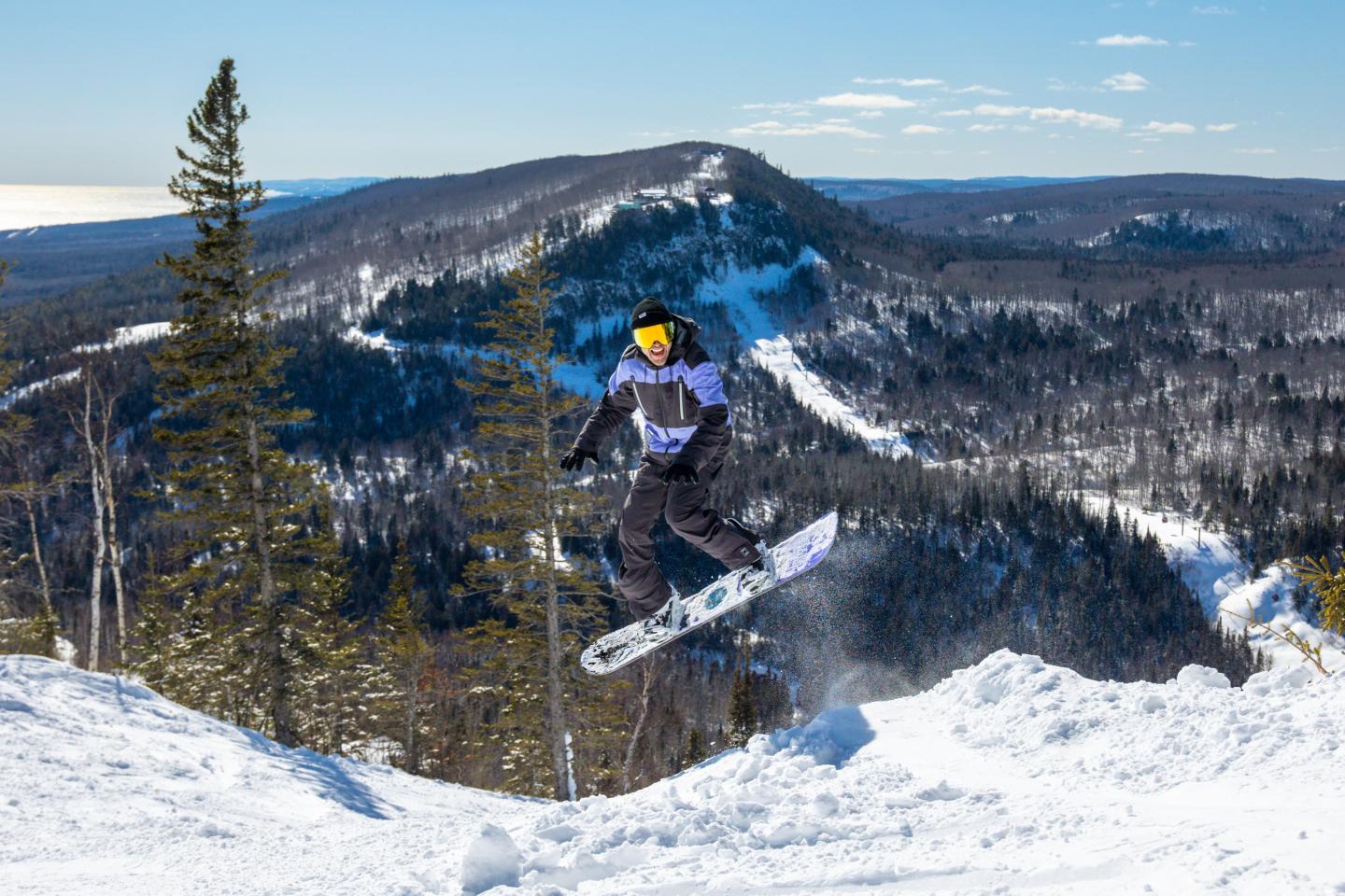 Snowboarder in mid-air, mountain backdrop, clear sky.