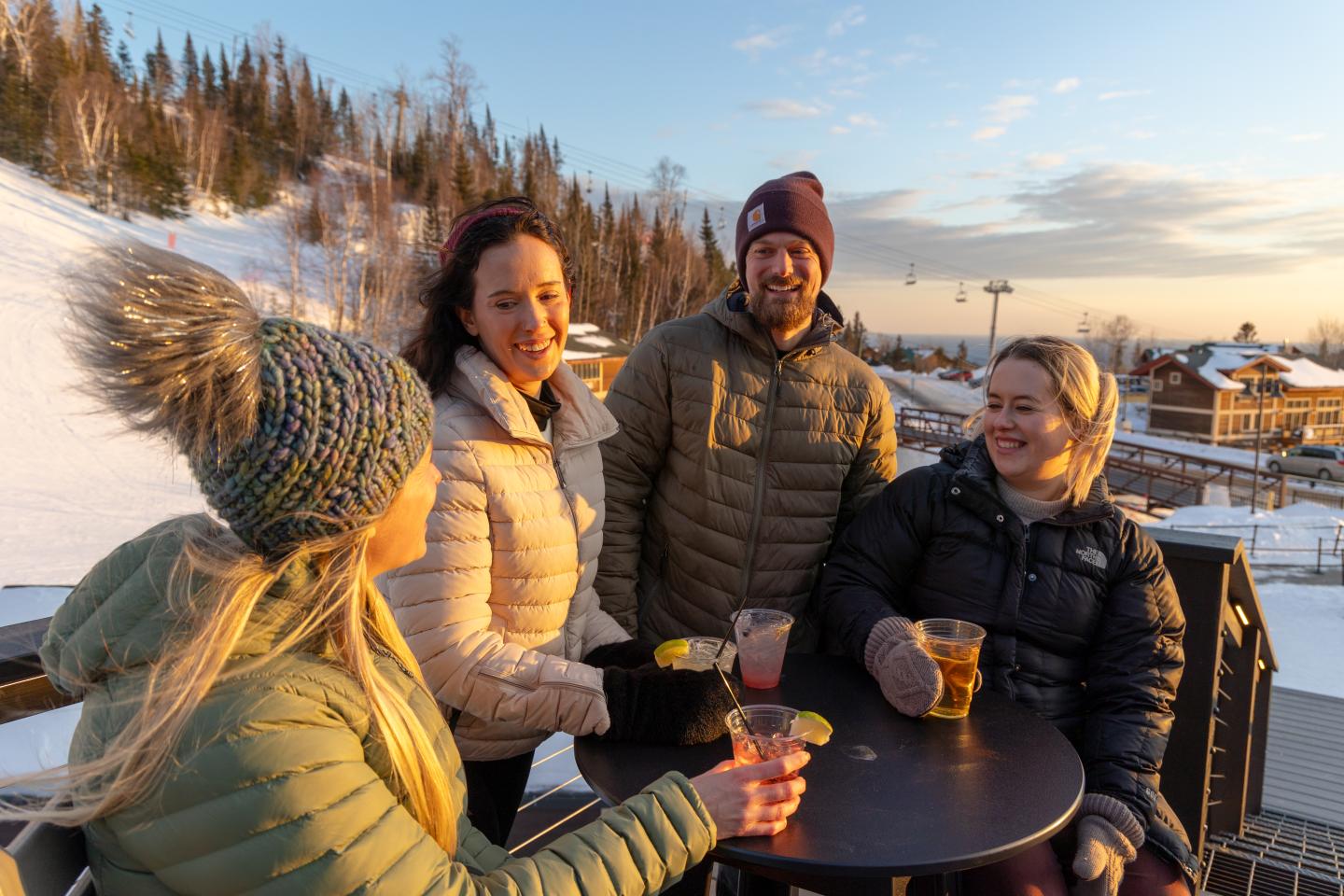 Group of friends in winter coats enjoying drinks outside at sunset.