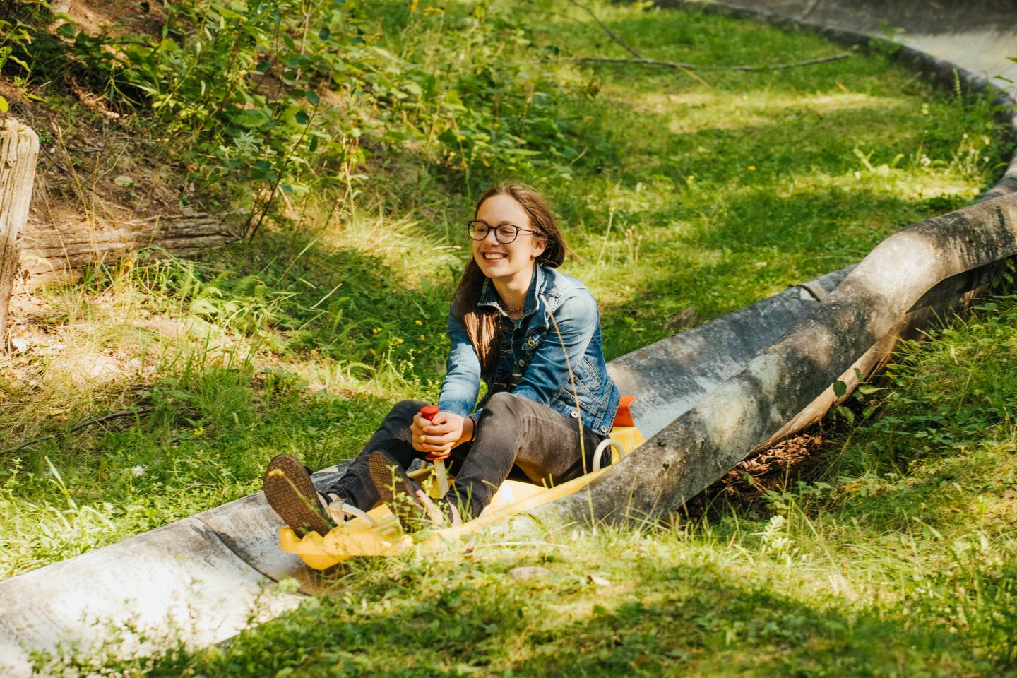 Woman joyfully riding a concrete slide in a grassy outdoor setting.