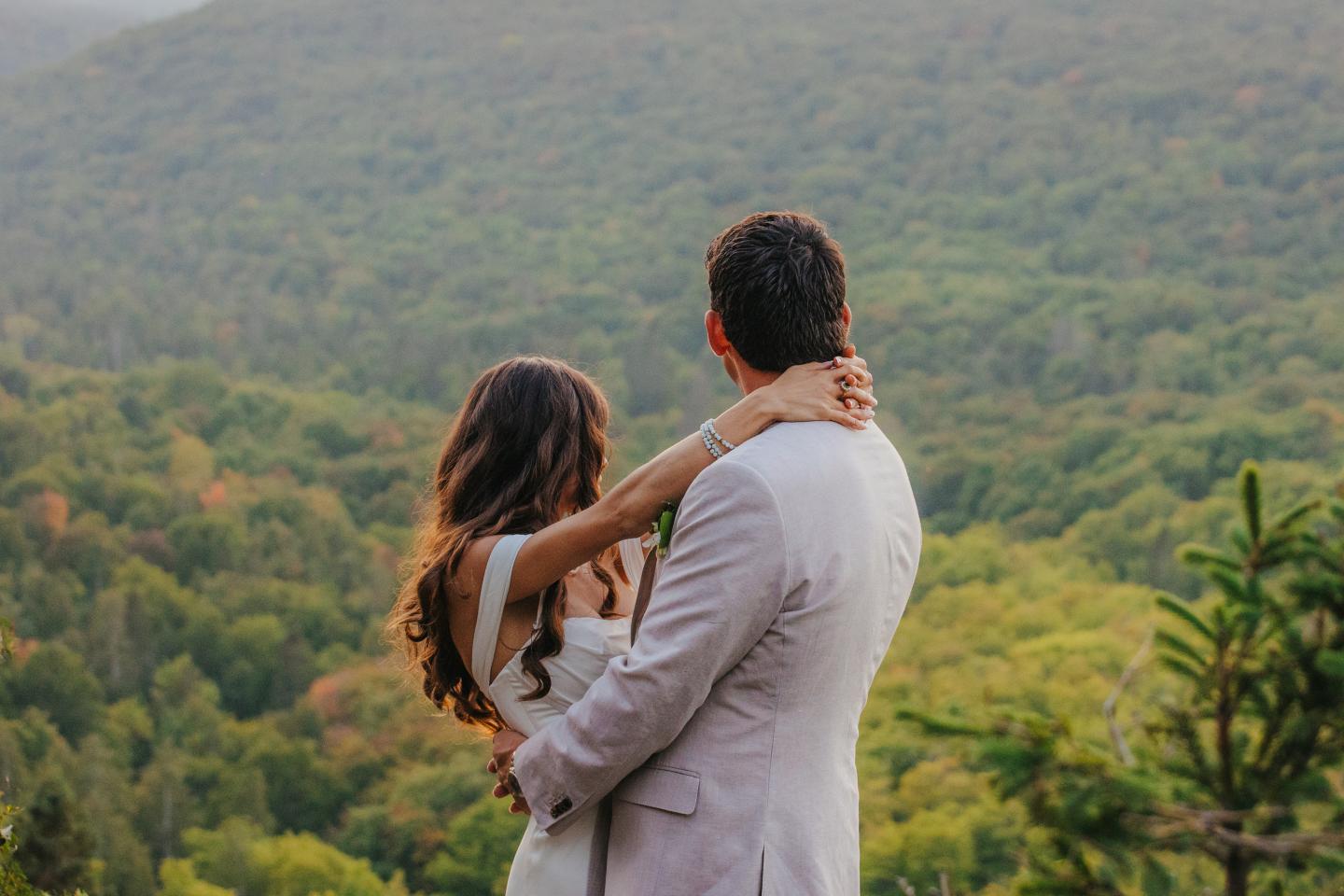 Couple embracing, gazing at a lush green forest and distant hills.