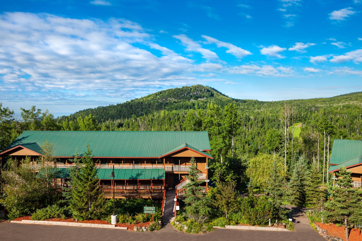 Lodge with green roof surrounded by trees, under a blue sky.