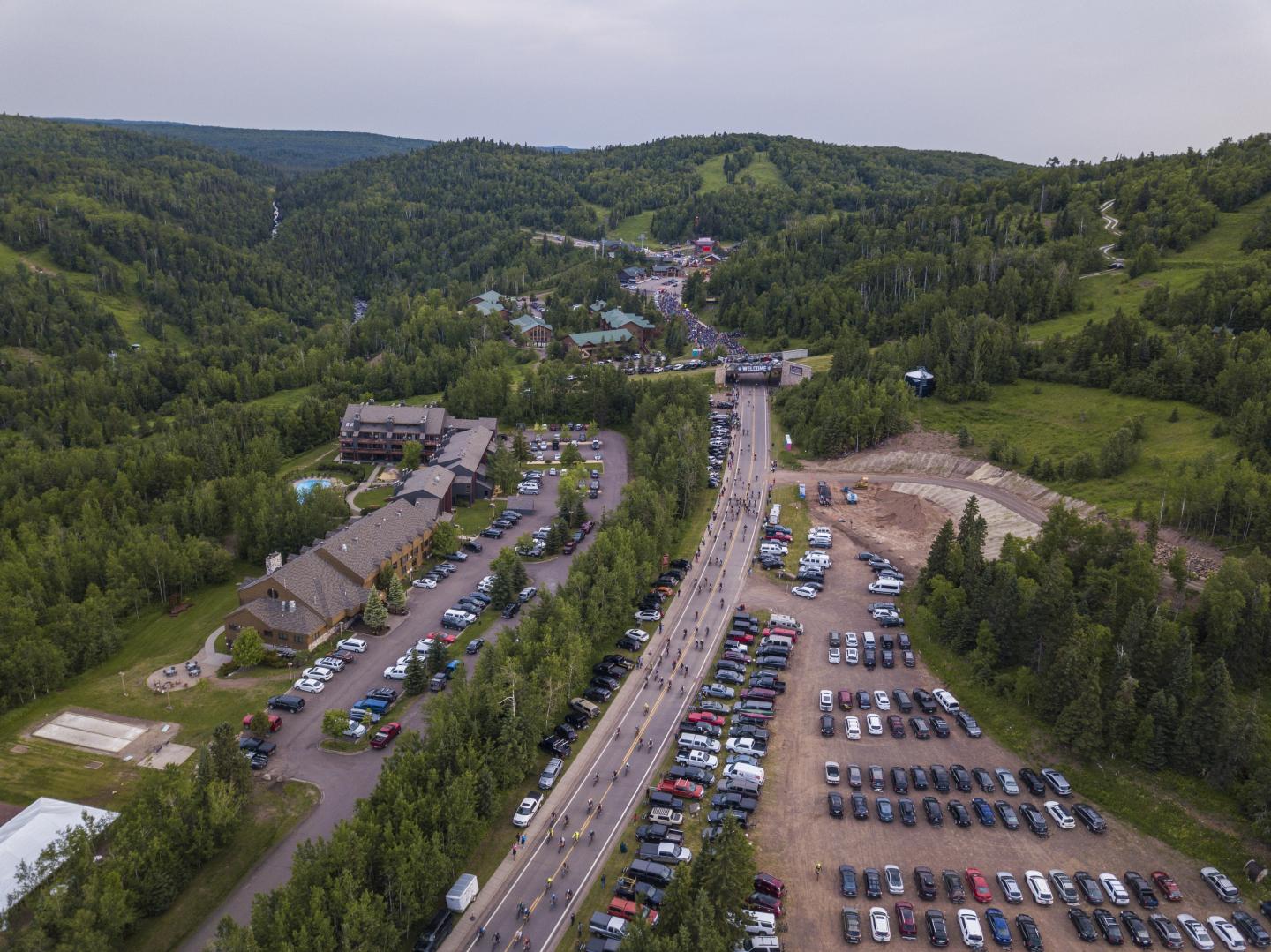 Aerial view of a parking lot and road in a green, hilly landscape.