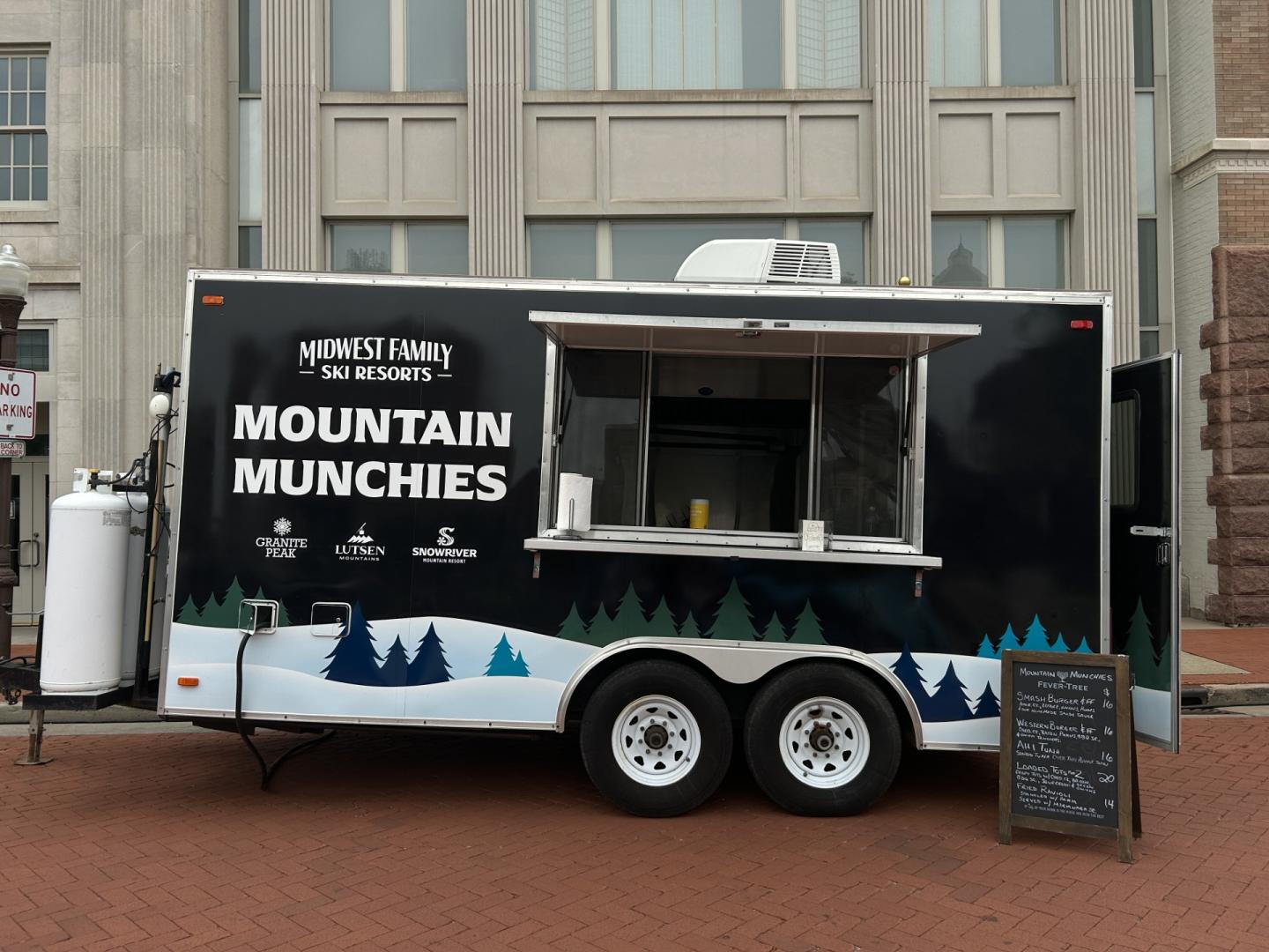Food truck with mountain-themed design parked on brick pavement.