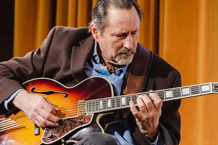 Man playing a sunburst electric guitar with focus and concentration.