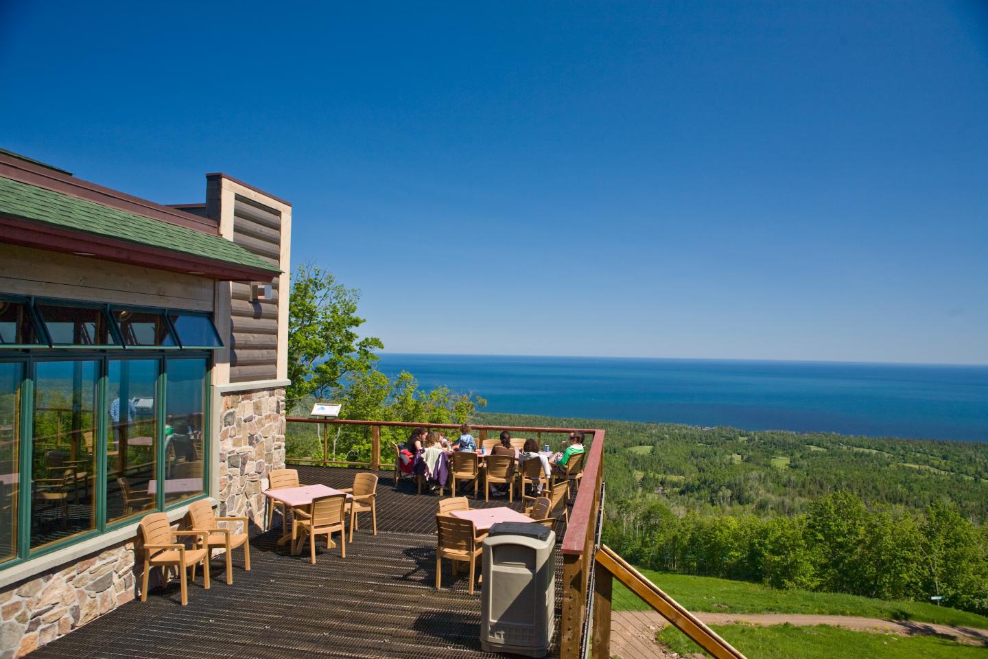 Restaurant patio overlooking ocean and greenery under clear blue sky.
