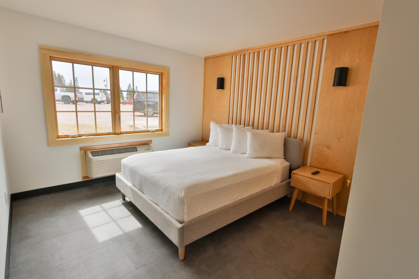 Minimalist bedroom with a double bed, wooden accents, and a large window.