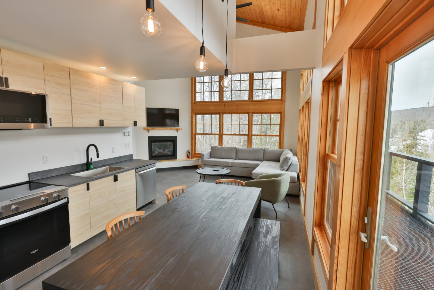 Modern kitchen and living room with large windows and wooden accents.