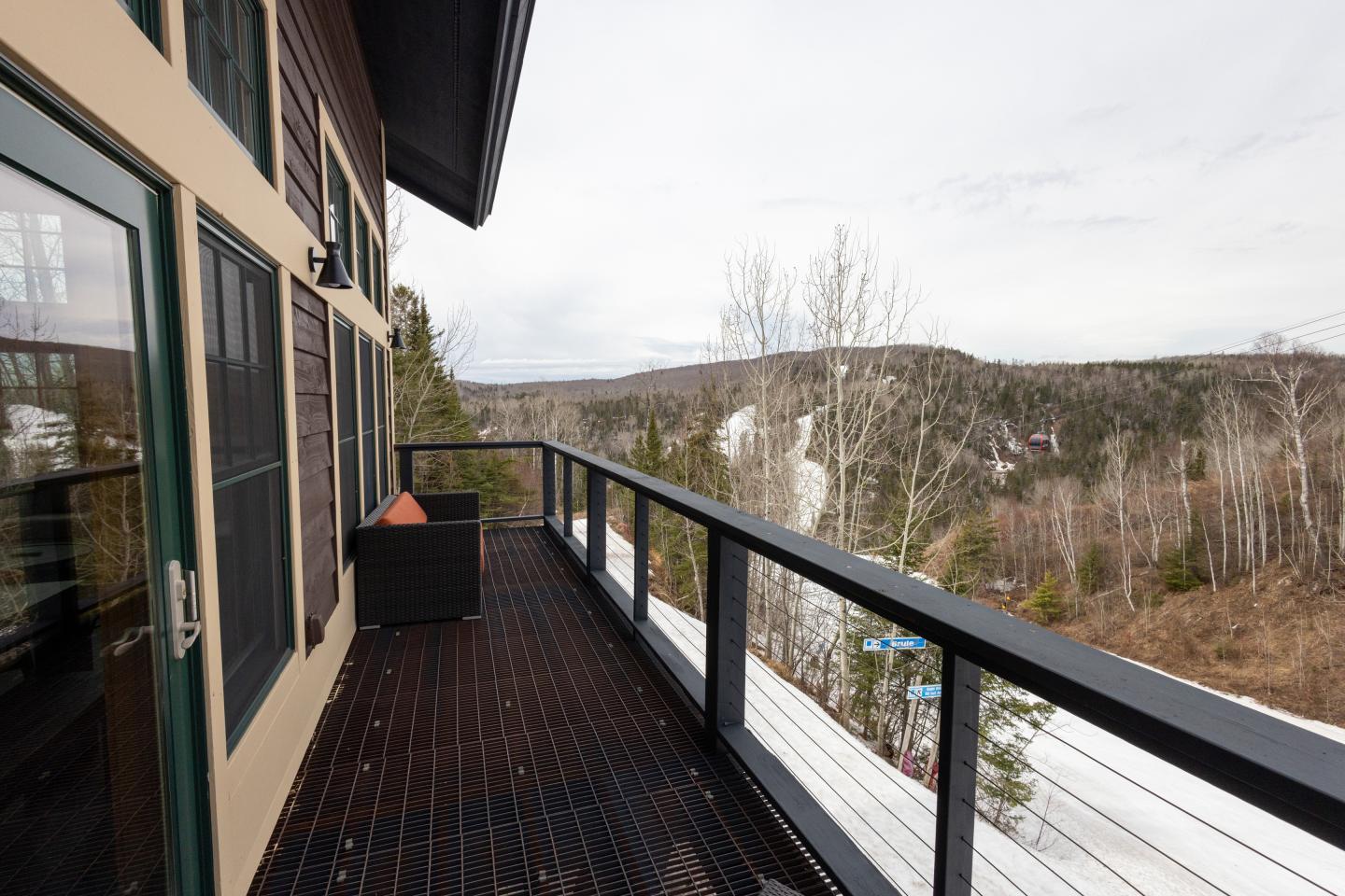 Wooden deck overlooking a snowy forest landscape with distant hills.